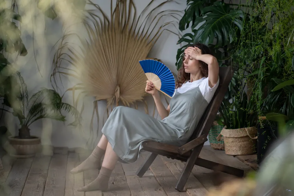young-woman-waving-with-paper-fan-while-sitting-home-garden-filled-with-tropical-foliage-plants How Long Do Hangovers vs. Withdrawal Last?