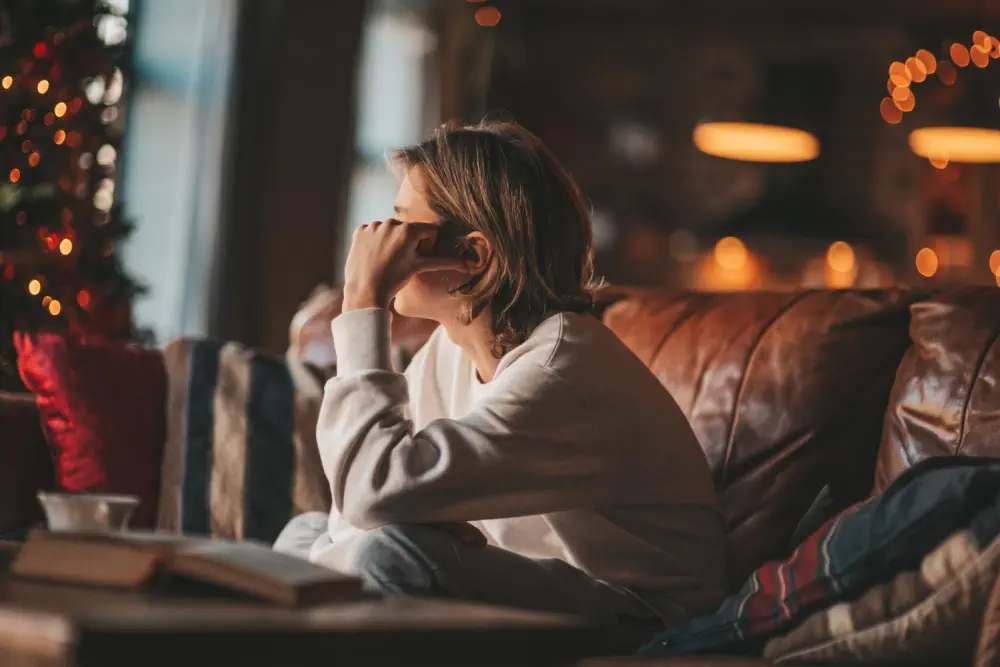 Person sitting sadly on a couch by a window during the holidays.
