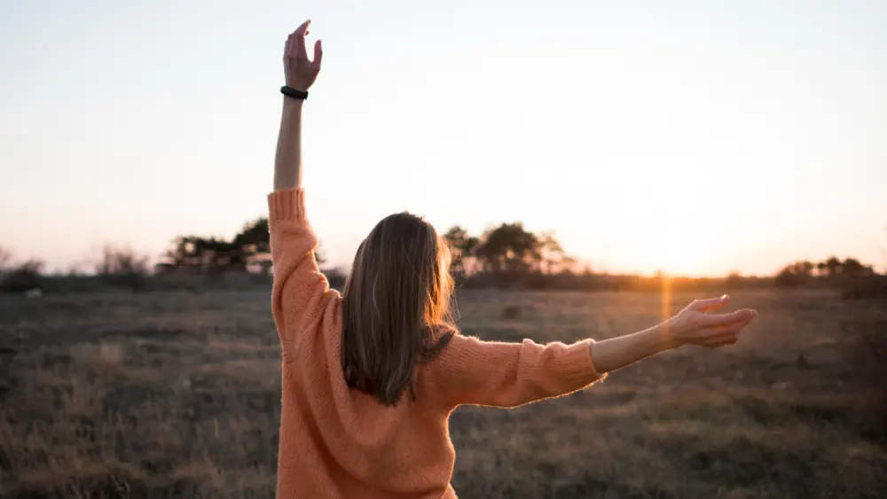 Woman with arms raised toward a sunset, symbolizing recovery and support.